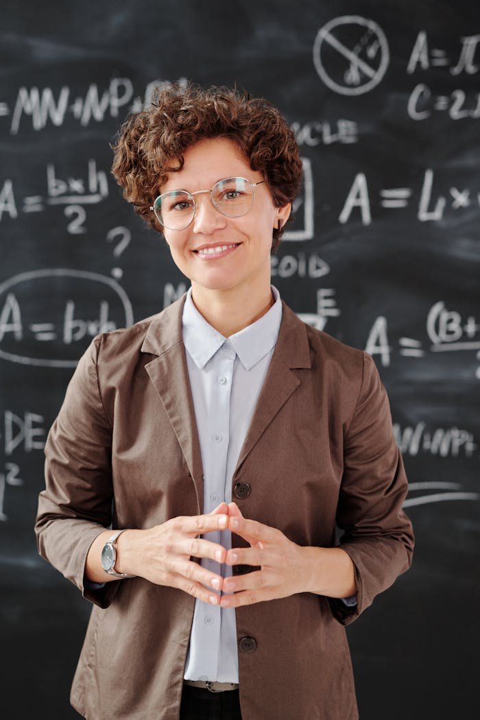 contact-img Teacher standing by a blackboard with algebra equations, smiling confidently.